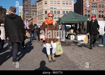 Une femme shopper sacs à transporter promenades à travers e Union Square Green Market à Manhattan sur un après-midi d'hiver ensoleillé. Banque D'Images