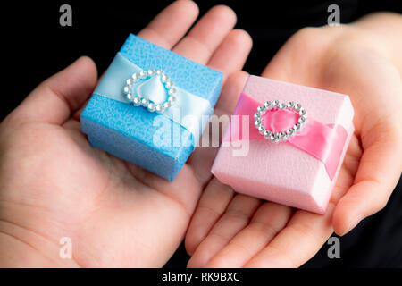 Homme et femme mains tenant cadeaux rose et bleu avec ruban rose et bleu sur fond noir mise à plat. Présent pour un anniversaire, la Saint-Valentin, Ch Banque D'Images
