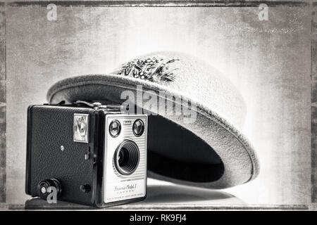 Gros plan noir et blanc de l'ancien chapeau Fedora/trilby des années 1950, appuyé sur l'ancien appareil photo Kodak Box Brownie (modèle 1) de la même période. Arrière-plan d'effet vieilli. Banque D'Images