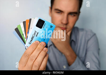 Le jeune homme est maintenant un arrêt des cartes de crédit et de débit dans une pose pensive. Le mec choisit une carte de paiement. businessman détient une grande pile de credit Banque D'Images