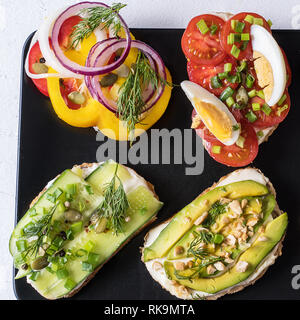 Choix de sandwichs avec du pain , fromage à la crème, les légumes et les ingrédients savoureux. Aliments biologiques sains pour le déjeuner ou petit déjeuner, sur la plaque noire, sur le Banque D'Images