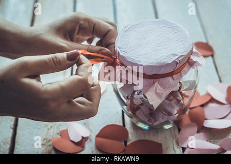 Lover's day. Pot en verre d'ouverture ou de date et désirs ou souhaits. Coeurs en papier rouge à l'arrière-plan. Banque D'Images