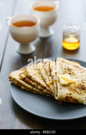 Les crêpes sur une plaque en céramique gris servi avec du miel et 2 tasses de thé. Table en bois sombre, haute résolution Banque D'Images