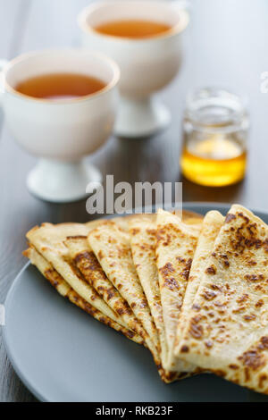 Les crêpes sur une plaque en céramique gris servi avec du miel et 2 tasses de thé. Table en bois sombre, haute résolution Banque D'Images