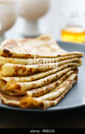 Les crêpes sur une plaque en céramique gris servi avec du miel et 2 tasses de thé. Table en bois sombre, haute résolution Banque D'Images