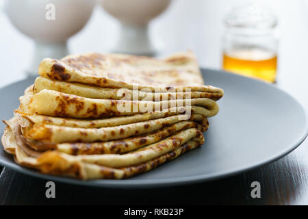 Les crêpes sur une plaque en céramique gris servi avec du miel et 2 tasses de thé. Table en bois sombre, haute résolution Banque D'Images