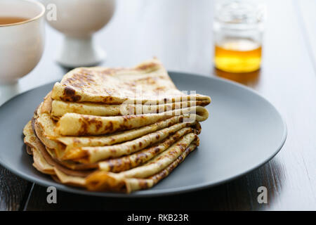 Les crêpes sur une plaque en céramique gris servi avec du miel et 2 tasses de thé. Table en bois sombre, haute résolution Banque D'Images