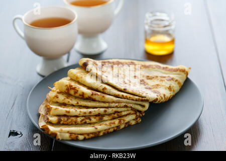 Les crêpes sur une plaque en céramique gris servi avec du miel et 2 tasses de thé. Table en bois sombre, haute résolution Banque D'Images