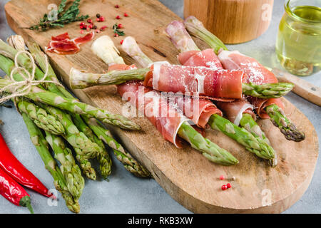 Asperges fraîches biologiques enveloppés dans du jambon prosciutto sur une planche à découper. Banque D'Images