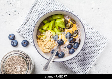 Petit-déjeuner végétalien. Chia pudding avec les kiwis, les bleuets et le beurre d'arachide dans un bol gris. Banque D'Images