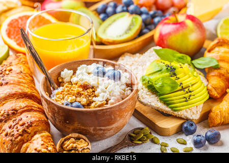 Petit-déjeuner sain et équilibré sur un fond blanc. Muesli, jus, pain grillé à l'avocat, des croissants, du fromage, des biscuits et des fruits. Banque D'Images