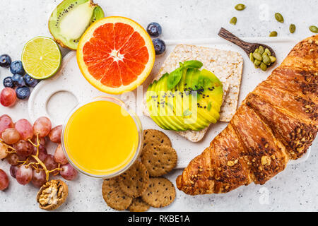 Le petit-déjeuner végétarien sain avec croissant, pain grillé, fruits d'avocat et de jus sur une assiette blanche, vue du dessus. Banque D'Images