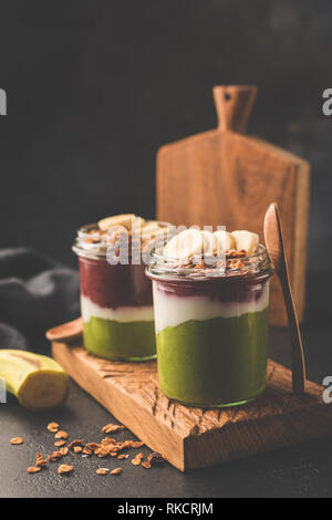 Smoothie arc-en-ciel dans un pot pour le petit-déjeuner. Detox saine smoothie ou végétalien parfait surmonté de granola et banana Banque D'Images