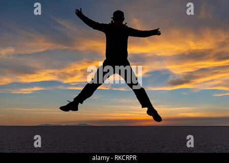 Jump shot avec la silhouette d'un jeune homme et touristique dans l'Uyuni Salt Flat (Salar de Uyuni) au coucher du soleil, la Bolivie. Banque D'Images