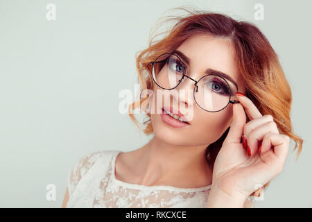 Jeune femme blonde frisée européenne holding lunettes rondes. Banque D'Images