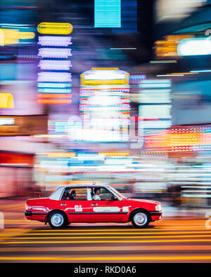 Les néons sont dynamiques dans l'ensemble de Hong Kong, un Taxi rouge vitesse dans une intersection à Kowloon, Hong Kong. Les taxis sont un moyen abordable de faire la navette. Banque D'Images