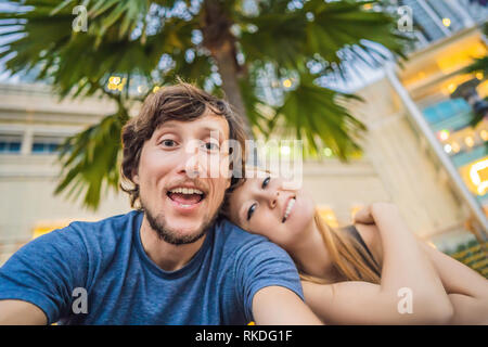 Les voyages, vacances et maison de vacances - concept heureux couple en tenant plus de selfies parc avec palmiers et gratte-ciel en arrière-plan. Banque D'Images