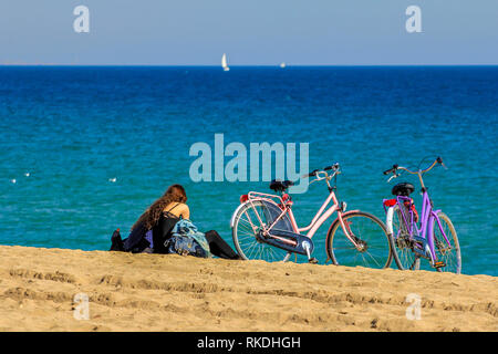 Portrait de deux jeunes filles couple assis sur le sable au bord de la mer avec des vélos garés à côté d'eux Banque D'Images