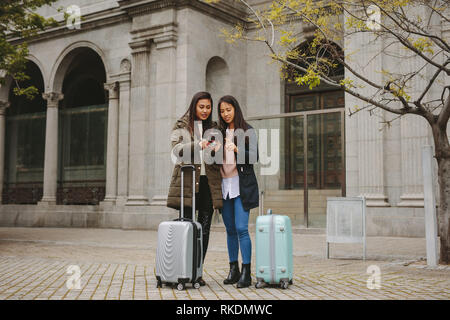 Deux femmes asiatiques les touristes à la recherche de téléphone mobile pour la navigation. Les femmes qui l'article dans rue avec valises à directions in cell p Banque D'Images