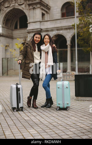 Deux touristes asiatiques standing in street tenant leurs valises. Femmes gaies de touristes en hiver vêtements aller autour de la ville. Banque D'Images