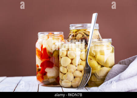 Champignons marinés, artichauts et divers légumes dans un pot en verre blanc sur fond de bois. Selective focus Banque D'Images