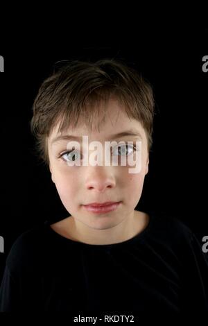 Portrait d'un enfant à la grave avec une coupe de cheveux pixie sur un fond noir Banque D'Images