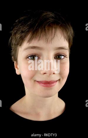 Portrait d'un enfant souriant avec une coupe de cheveux pixie sur un fond noir Banque D'Images