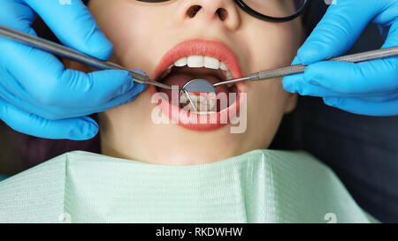 Examen de routine chez le dentiste. Jeune fille avec la bouche ouverte. Des dents blanches. Dentiste de mains dans des gants avec miroir et crochet outil médical. Clos Banque D'Images