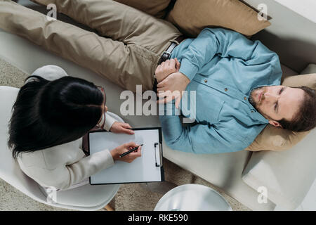 Vue de dessus de psychothérapeute writing on clipboard et male patient lying on couch Banque D'Images