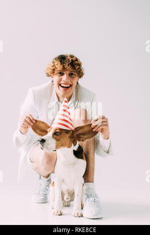 Homme heureux avec les cheveux bouclés tenant les oreilles de mignon chien beagle sur fond gris Banque D'Images