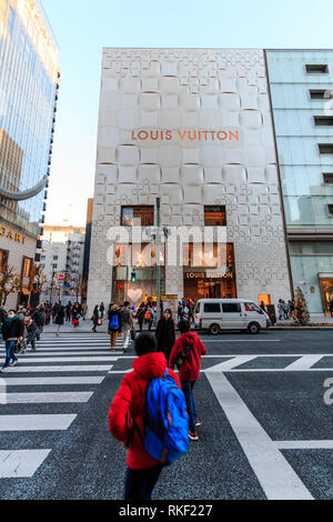 Tokyo, le Ginza. Premier plan, les personnes qui franchissent le passage piétons avec l'édifice du magasin Louis Vuitton de l'autre côté de la rue. Jour, heure d'or. Banque D'Images