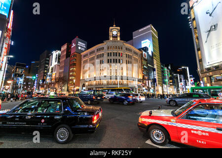 Tokyo, Ginza, nuit. 4-chome intersection avec le trafic et les taxis passant par motion, bleu, et en arrière-plan l'Wako Department store et d'autres. Banque D'Images