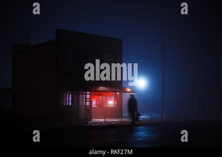 Bleu nuit paysage brumeux. Une petite boutique avec un panneau lumineux rouge se tient sur le côté de la route, une silhouette d'un homme gras traverse la Banque D'Images