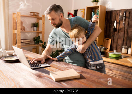 Le père moderne essaie de travailler et s'occuper de son fils Banque D'Images