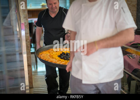 Un chef porte une paella fraîchement préparés par un restaurant à Valence, en Espagne. Banque D'Images