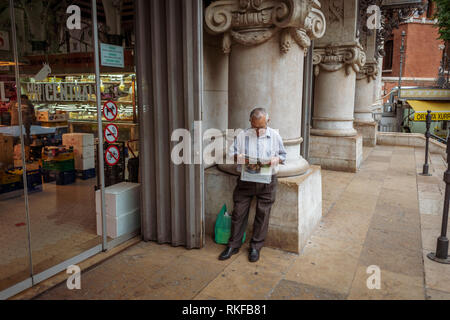 Un homme lit un journal tout en s'appuyant sur un pilier à l'extérieur du Marché Central, du Marché Central, à Valence, Espagne. Banque D'Images