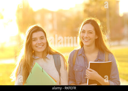 Vue avant portrait de deux professionnels d'étudiants à la recherche à l'appareil photo au coucher du soleil dans un parc Banque D'Images