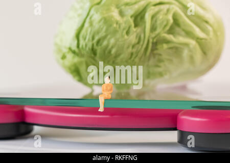 Femme miniature figure l'emplacement de l'électronique numérique balance de salle pour les poids de corps humain. Des légumes frais à faible profondeur de champ background Banque D'Images