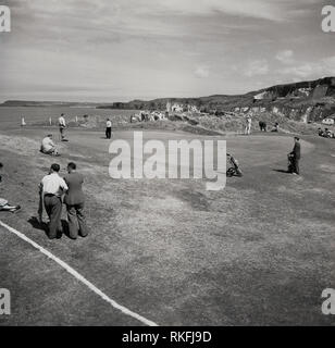 1951, golfeur et caddy avec drapeau sur le green du British Open Golf Championship, à l'Liens Dunluce au Royal Golf Club Portrrush, Co Antrim, en Irlande du Nord. Ouvert en 1888, ce parcours de golf sur la côte de Causeway à North Antrim est due à l'attente 2019 Championnat ouvert, le seul cours en dehors de la partie continentale de l'attente de l'événement. Banque D'Images