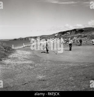 1951, golfeur et caddy avec drapeau sur le green du British Open Golf Championship, à l'Liens Dunluce au Royal Golf Club Portrrush, Co Antrim, en Irlande du Nord. Ouvert en 1888, ce parcours de golf sur la côte de Causeway à North Antrim est due à l'attente 2019 Championnat ouvert, le seul cours en dehors de la partie continentale de l'attente de l'événement. Banque D'Images