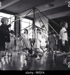 Années 1960, historiques, des enfants qui jouent un jeu de 'ring-a-ring-a-roses' dans une salle d'école, England, UK. Une pépinière traditionnelle chanson, le jeu voit un un groupe d'enfants formant un anneau ou cercle pour danser ou sauter autour d'un poteau. Banque D'Images