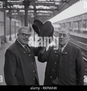 Joyeux 1968, deux employés de la station ferroviaire britannique en uniforme, un contremaître et contrôleur debout sur une plate-forme à la gare de Blackheath, soulever leur casquette, Blackheath, Londres, Angleterre, Royaume-Uni. Banque D'Images