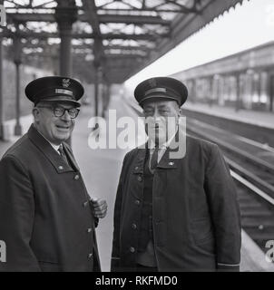 1968, deux employés de la station ferroviaire britannique en uniforme, un contremaître et contrôleur debout ensemble sur une plate-forme à la gare de Blackheath, Blackheath, Londres, Angleterre, Royaume-Uni. Banque D'Images