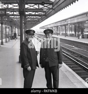 1968, deux employés de British Rail en uniforme, un contremaître et collectionneur ticket station debout ensemble sur une plate-forme vide au Blackheath railway station, Blackheath, Londres, Angleterre, Royaume-Uni. Banque D'Images