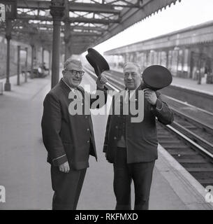 1968, deux membres du personnel en uniforme joyeuse British Rail Station, un contremaître et contrôleur, debout sur la plate-forme à la gare de Blackheath, soulever leur casquette, Blackheath, Londres, Angleterre, Royaume-Uni. Banque D'Images