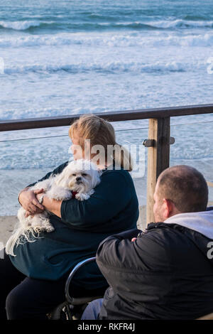 Une femme, berçant un shih tzu chien et assis sur un balcon donnant sur la mer à dans Fistral Newquay Cornwall. Banque D'Images