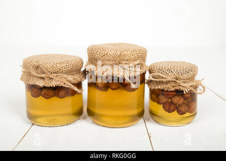 Les noisettes avec du miel dans des bocaux en verre blanc sur les planches de bois. Délicatesse sucrée délicieuse. Banque D'Images