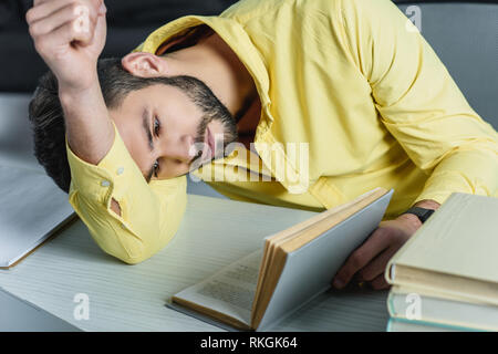 Homme fatigué d'étudier avec book while lying on table in modern office Banque D'Images