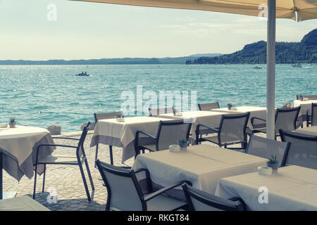 Café sur le bord de la mer ou du lac, des tables couvertes de nappes blanches avec des cendriers et pots décoratifs sur une journée ensoleillée, debout dans le sh Banque D'Images