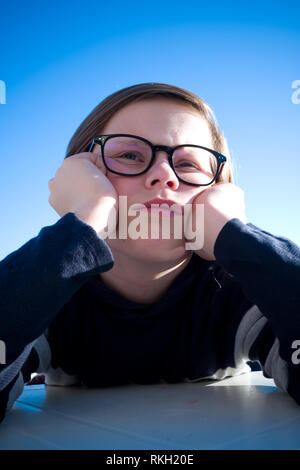 Portrait d'un garçon de onze ans assis avec des lunettes reposant sa tête dans ses mains, tandis que dans la pensée profonde et à la grognon Banque D'Images